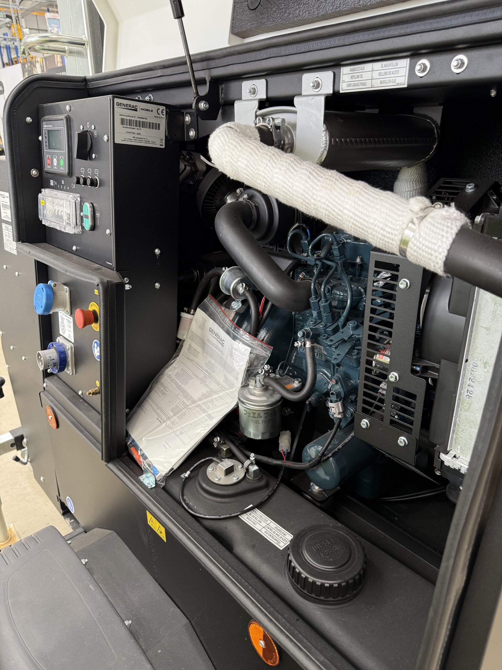 Open service compartment of a Generac Mobile diesel generator showing the engine, control panel, alternator, exhaust system, fuel filter, and cooling components. The industrial generator feat