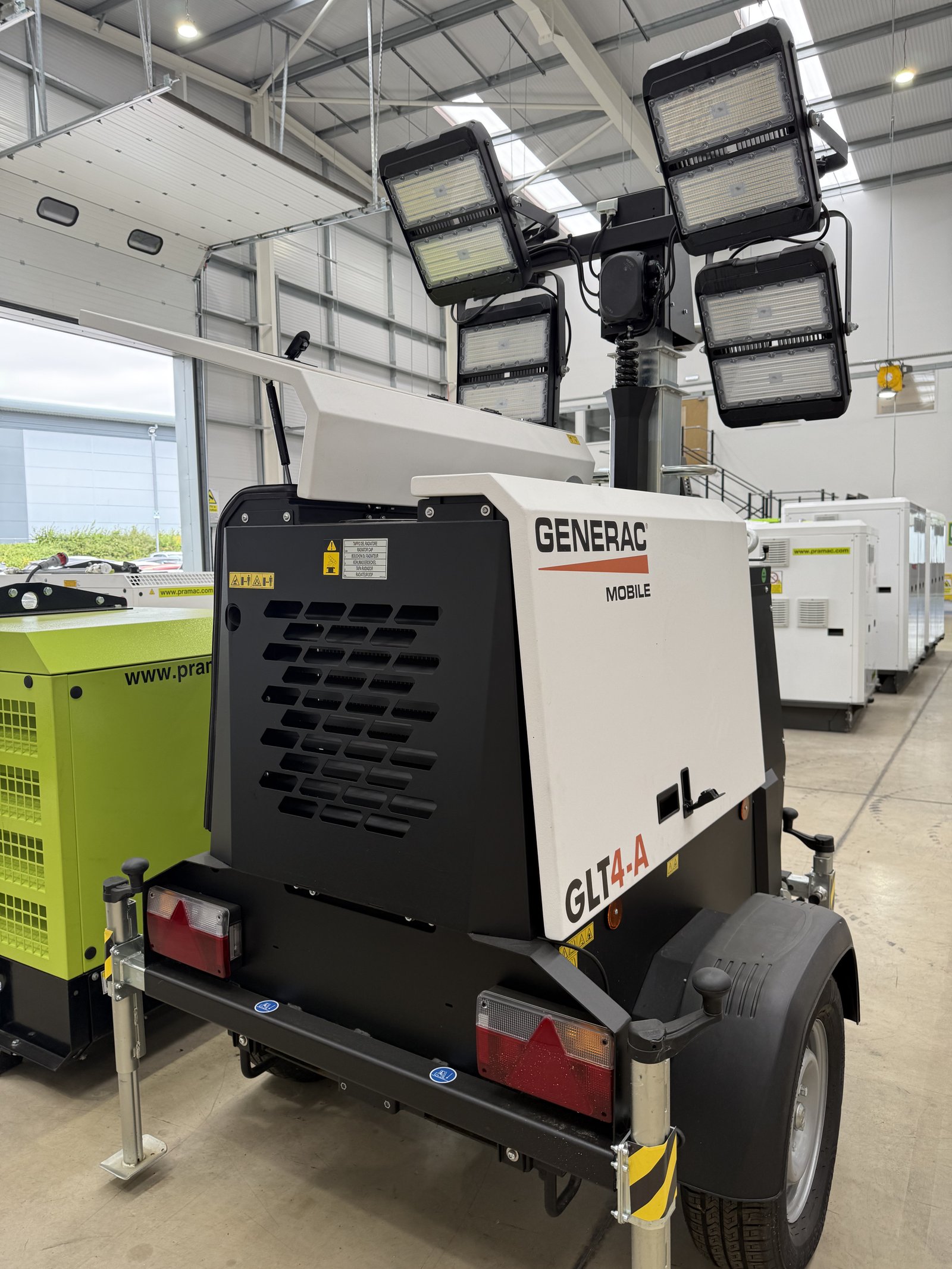 Rear view of a Generac Mobile GLT4-A LED lighting tower inside a modern warehouse. The towable mobile light tower features four high-output adjustable LED floodlights mounted on a telescopic 