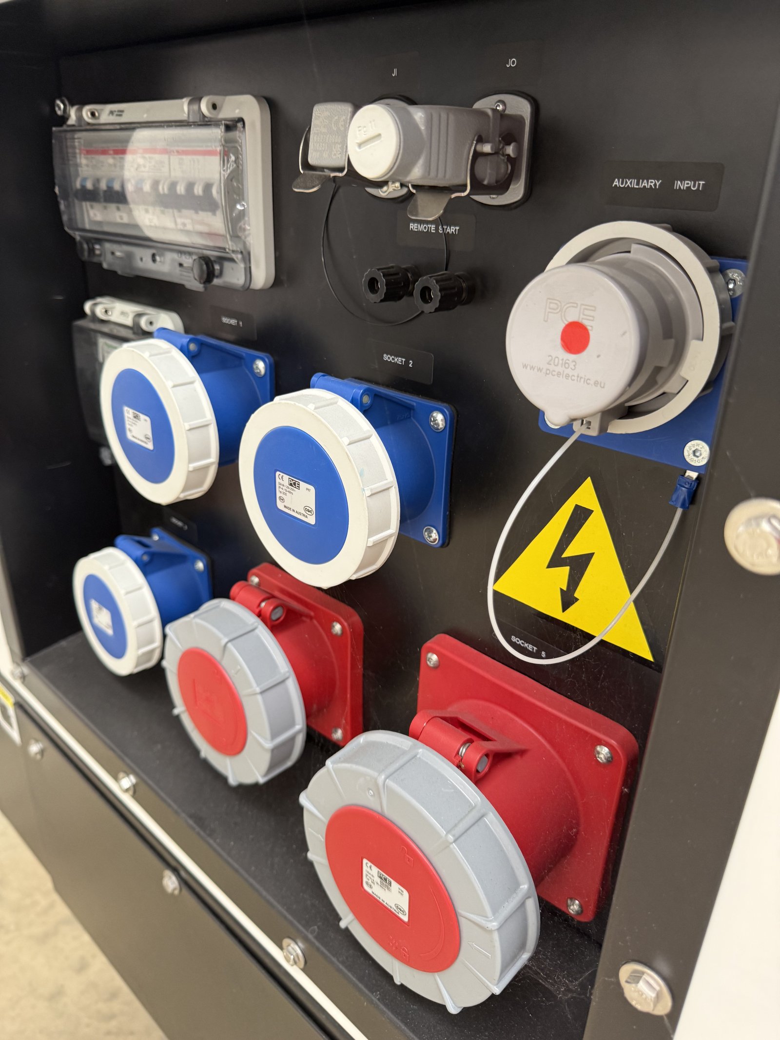 Close-up of an industrial generator power output panel featuring multiple 230V and 400V CEE industrial sockets, auxiliary input connection, remote start interface, circuit breakers, and elect